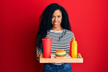 Sticker - Middle age african american woman eating a tasty classic burger smiling with a happy and cool smile on face. showing teeth.