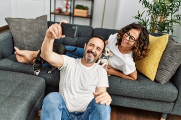 Wall Mural - Middle age hispanic couple smiling happy and making selfie by the smartphone. Sitting on the sofa with dogs at home.