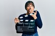 © Krakenimages.com - Young hispanic woman holding video film clapboard covering mouth with hand, shocked and afraid for mistake. surprised expression