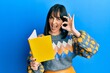 © Krakenimages.com - Young hispanic woman reading book doing ok sign with fingers, smiling friendly gesturing excellent symbol