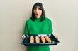 © Krakenimages.com - Young hispanic woman holding homemade bread afraid and shocked with surprise and amazed expression, fear and excited face.