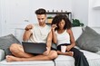 © Krakenimages.com - Young interracial couple using laptop at home sitting on the sofa pointing down with fingers showing advertisement, surprised face and open mouth