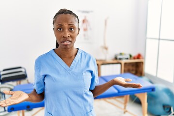 Canvas Print - Black woman with braids working at pain recovery clinic clueless and confused with open arms, no idea concept.