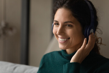 Wall Mural - Digital headphones. Close up shot of smiling young latina woman wearing modern wireless earphones talking to customer online by video call. Skilled female interpreter translate virtual event remotely