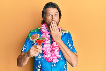 Canvas Print - Middle age handsome man wearing hawaiian lei drinking cocktail covering mouth with hand, shocked and afraid for mistake. surprised expression