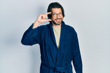 Sticker - Middle age caucasian man wearing bathrobe and glasses smiling and confident gesturing with hand doing small size sign with fingers looking and the camera. measure concept.