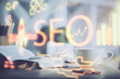 © peshkova - Double exposure of SEO writing and desktop with coffee and items on table background. Concept of search optimization.