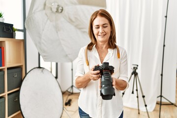 Poster - Middle age caucasian woman photographer smiling confident holding professional camera at photograph studio