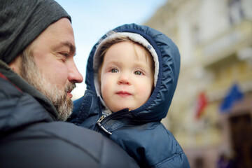 Sticker - Cute little baby boy in his fathers arms. Dad and son having fun on chilly winter day in city park.