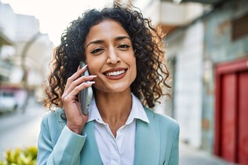 Wall Mural - Young hispanic business woman wearing professional look smiling confident at the city speaking on the phone