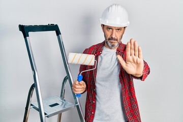 Poster - Middle age hispanic painter man holding roller using ladder with open hand doing stop sign with serious and confident expression, defense gesture