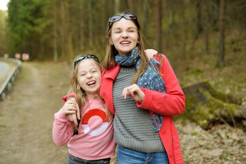 Wall Mural - Two cute young sisters having fun during forest hike on beautiful early spring day. Active family leisure with kids.