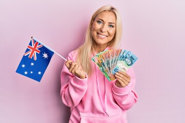 Poster - Young blonde woman holding australian flag and dollars smiling with a happy and cool smile on face. showing teeth.