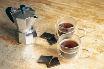 Coffee pot, two coffee glass cups and dark chocolate on wooden table