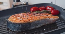 raw salmon steak fried in a grill pan. the chef prepares a steak. sprinkles it with salt and spices. the chef sauces the salmon steak on each side.