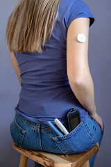 Girl sitting with flash glucose monitor, patch on her hand and monitor