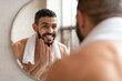 © Prostock-studio - Confident young Arab guy looking in the mirror, touching beard