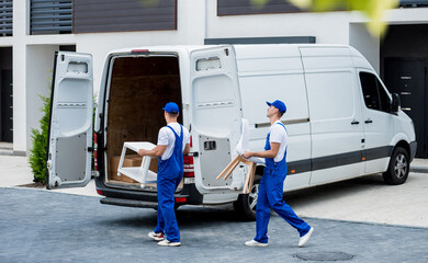 two removal company workers are loading boxes and furniture into a minibus.