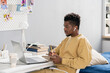 © pressmaster - Serious young student of African ethnicity making notes while listening to teacher on laptop display at lesson