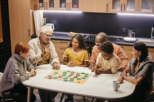 Large happy multiracial family of three generations playing board game while sitting by table in the kitchen