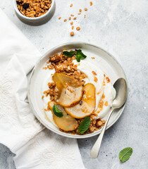 Wall Mural - Greek yogurt with caramelized pear, granola, nuts and melted sugar for a wholesome breakfast on a gray ceramic plate. Rustic style. Top view
