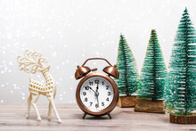 Christmas Background With Small Fir Trees And Vintage Alarm Clock And Deer On A Wooden Background With Lights. Close, Christmas Theme.