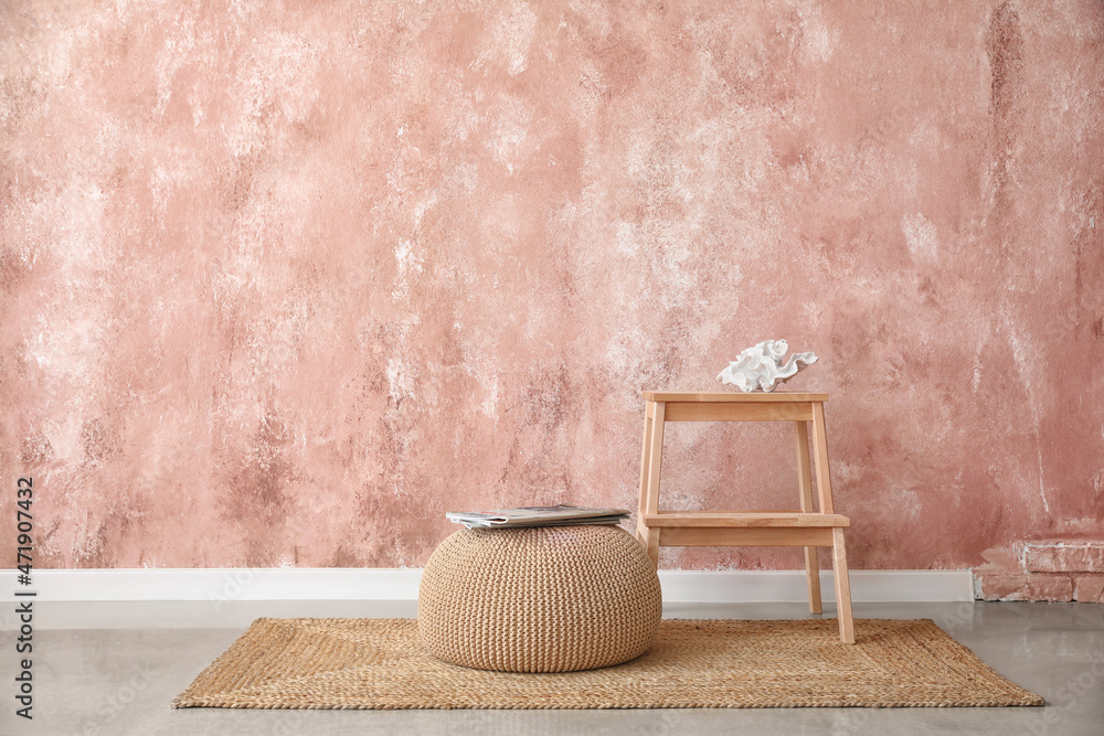 Wooden step stool and pouf with magazines near pink wall