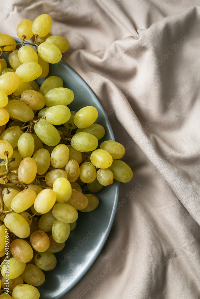 Plate with sweet ripe grapes on fabric background, closeup
