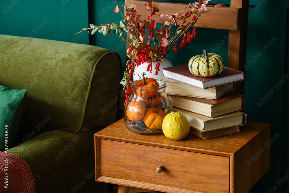 Books, pumpkins and vase with autumn branches on table in room