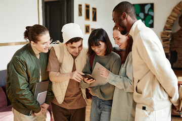 Wall Mural - Young smiling woman showing something on mobile phone to her classmates while they standing in the classroom