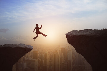 Poster - Man jumping from cliff on beautiful sky and city background. Gap, leap, risk, challenge and success concept.