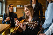 © Miljan Živković - Side view portrait of adult caucasian woman sitting at cafe with guitar on her lap playing holding accord singing to her friends - female musician relaxed real people leisure concept