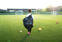 UK, Rear View Of Female Soccer Player (12-13) Carrying Bag With Balls In Field