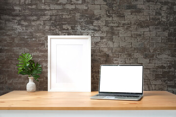 Wall Mural - mock up laptop computer, white picture frame and houseplant on wooden table with brick wall.
