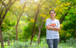 Portrait of Asian middle-aged woman posing in a park with casual clothes for exercise, standing with cross arms on chest, blurred background of trees in the park, blank space for text.