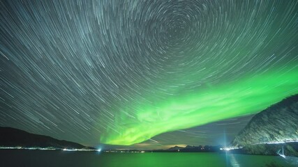Wall Mural - Starry sky and northern lights above the fjord. City lights in a distance. Full night timelapse.