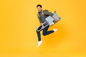 Portrait of jumping young excited Asian tourist man with baggage in isolated studio yellow background