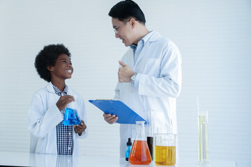 Wall Mural - Little African kid boy studying chemistry and doing chemical science experiment in laboratory at school. Happy dark skinned boy showing test bottle to Asian teacher man and he thumbs up with smile