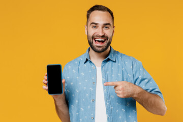 Sticker - Young smiling happy man 20s in blue shirt white t-shirt hold in hand use point index finger on mobile cell phone with blank screen workspace area isolated on plain yellow background studio portrait.