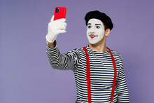 Fun Young Mime Man With White Face Mask Wears Striped Shirt Beret Doing Selfie Shot On Mobile Cell Phone Post Photo On Social Network Isolated On Plain Pastel Light Violet Background Studio Portrait.