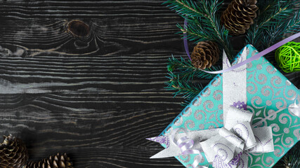 New Year's background gift in color packaging and decor of fir branches with pine cones on the background of a dark flatley tree