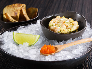 fresh scallop tartare, raw minced scallop with avocado and caviar of flying fish tobiko in a bowl on ice bed