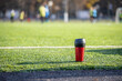 A red sports bottle with a black lid is located on a green football field made of synthetic grass.