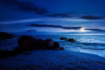 Wall Mural - huge stones on the sandy beach at night. wonderful velvet season vacation on the black sea in full moon light. calm waves washing the shore. clouds on the dark blue sky above horizon