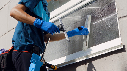 Wall Mural - Male professional cleaning service worker in overalls cleans the windows and shop windows of a store with special equipment