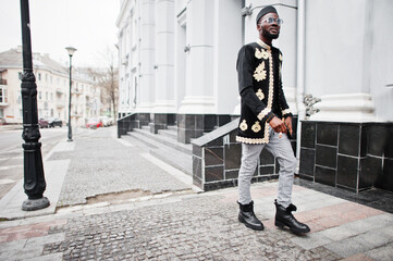 Wall Mural - Mega stylish african man in traditional jacket pose. Fashionable black guy in hat and sunglasses with cigar in hand.