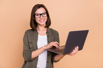 Wall Mural - photo of cheerful glad lady hold laptop prepare project wear eyewear khaki shirt isolated beige colo