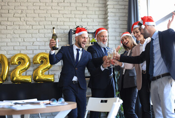 Wall Mural - Business people are celebrating holiday in modern office drinking champagne and having fun in coworking. Merry Christmas and Happy New Year 2022.