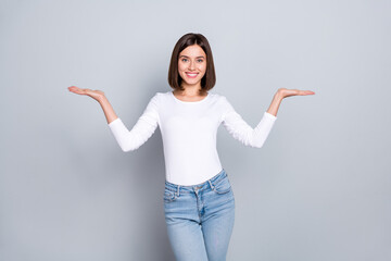 Wall Mural - Photo of charming cute young woman wear white outfit comparing arms empty space smiling isolated grey color background