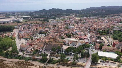 Wall Mural - Scenic summer view of tiled roofs of residential houses of Spanish township of Tordera on background of greenery of Montnegre natural park on horizon on sunny day, province of Barcelona, 